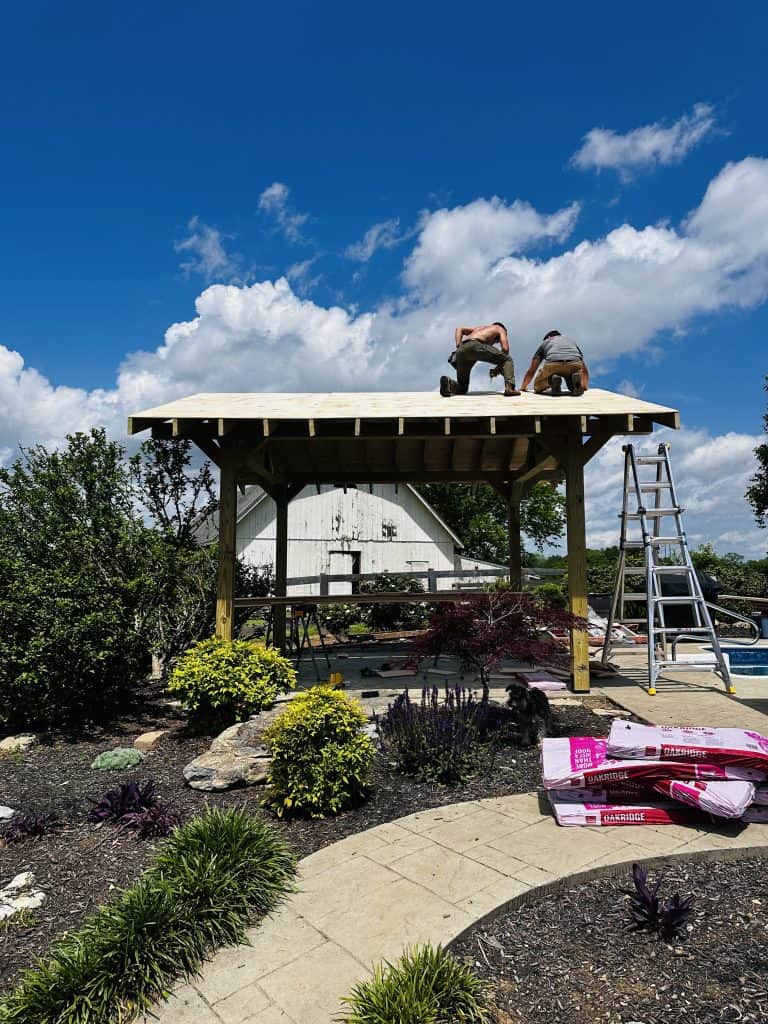 Custom outdoor pavilion construction in East Tennessee showing timber frame and roof decking installation in progress beside a pool