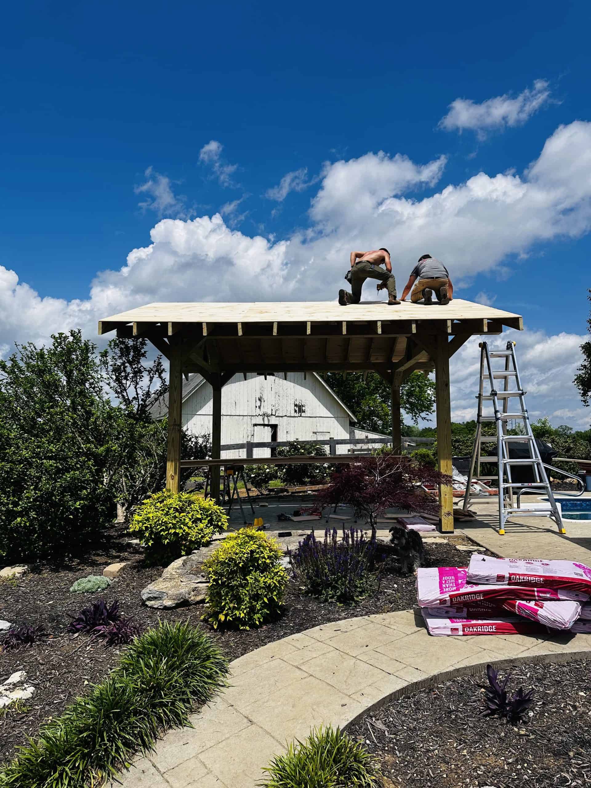 Custom outdoor pavilion construction in East Tennessee showing timber frame and roof decking installation in progress beside a pool