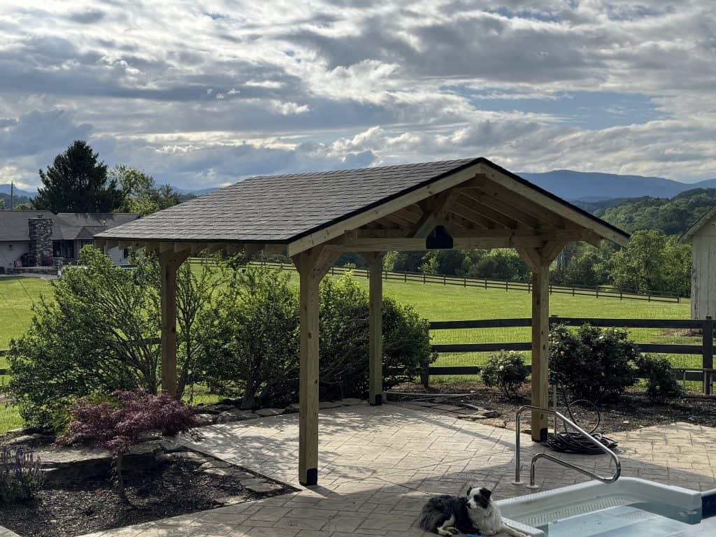 Completed custom poolside pavilion with solid pitched roof and heavy timber posts beside a pool patio in East Tennessee