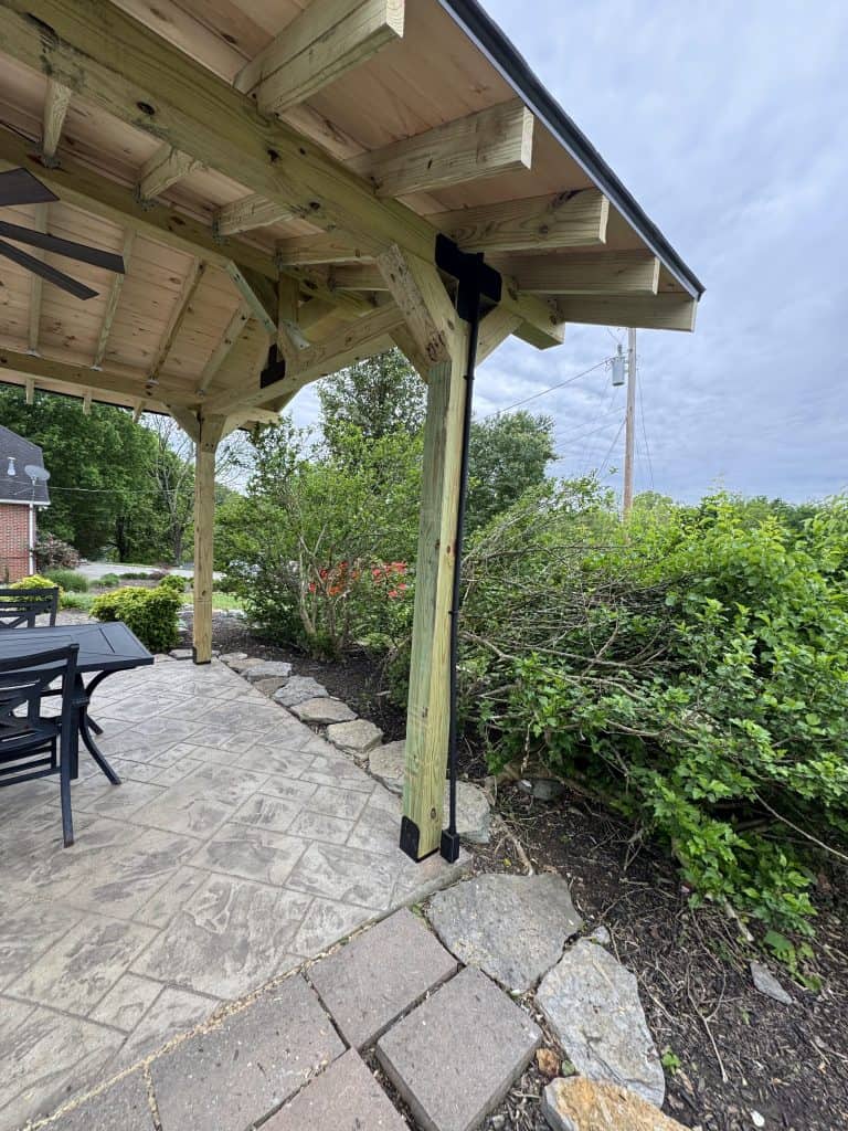 Timber frame pavilion post with black metal base bracket on stamped concrete patio with stone border edging and outdoor dining furniture in East Tennessee