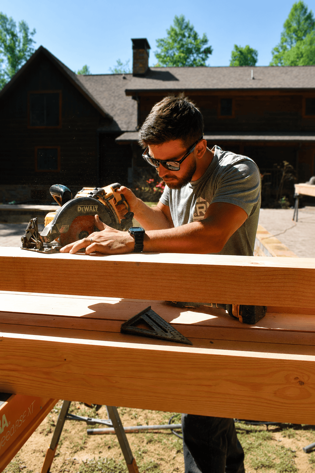 Jonathan Hodge using a circular saw to cut pergola framing lumber during an outdoor custom construction project in Knoxville Tennessee with luxury cabin home in the background