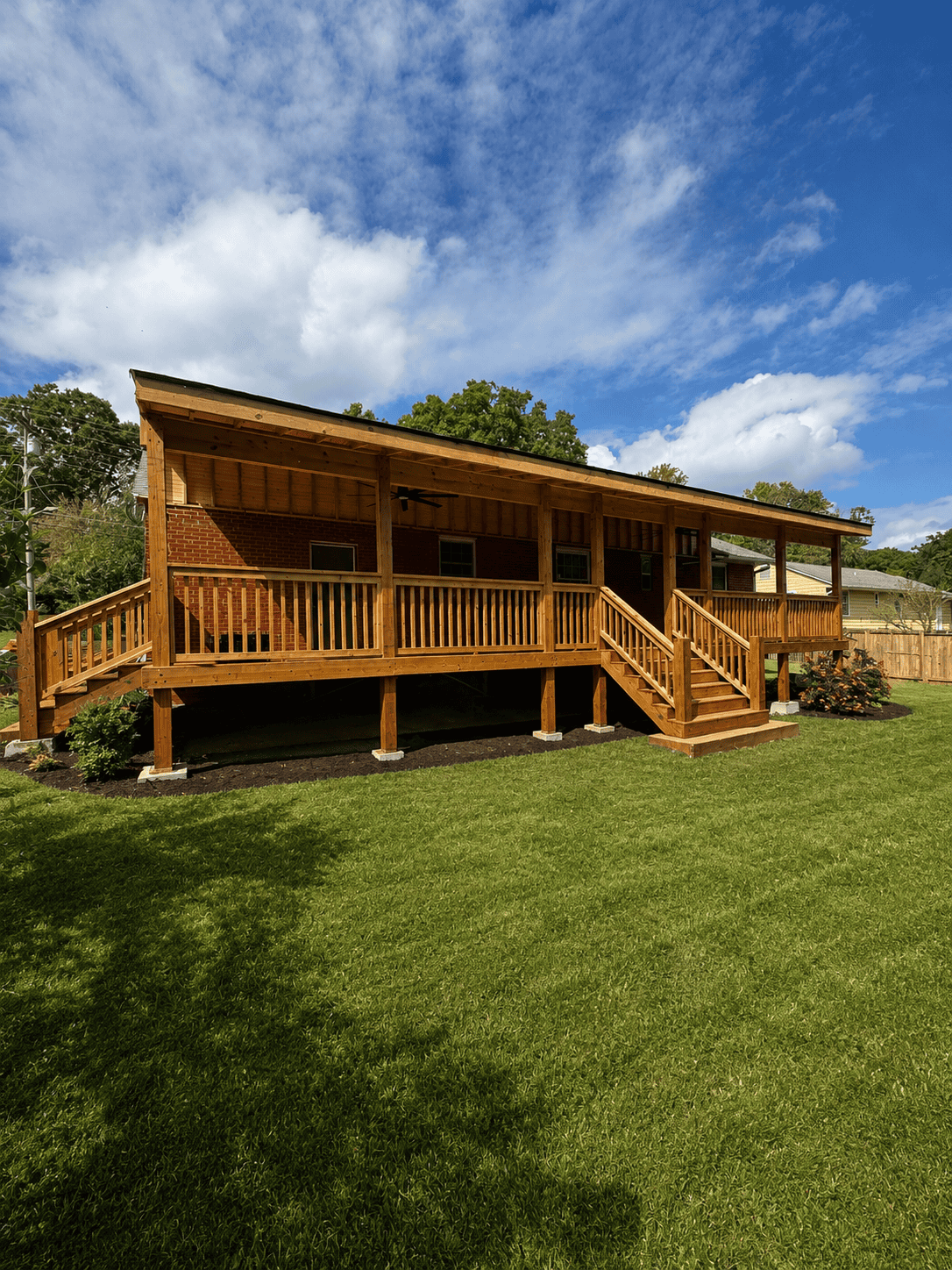 Custom full length covered back porch with stained wood deck, railings, dual staircases, and ceiling fan addition on brick home in Knoxville Tennessee