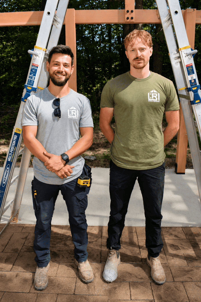 Logan Dixon and Jonathan Hodge Revival Properties team standing outdoors at a construction project site in front of a timber pergola structure wearing Revival Properties company shirts.