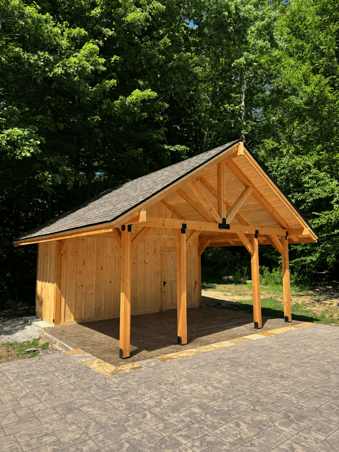 Custom timber frame pavilion with enclosed storage room, gabled shingled roof, black metal post brackets, and stamped concrete pad in East Tennessee