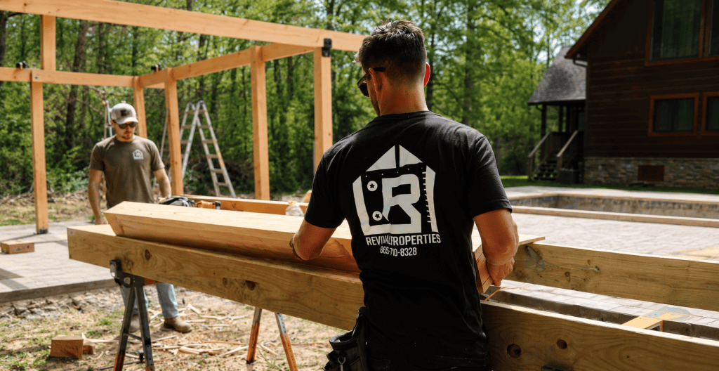 Revival Properties team members building a custom pergola structure outdoors with large timber beams and luxury craftsmanship in a wooded residential setting near Knoxville Tennessee