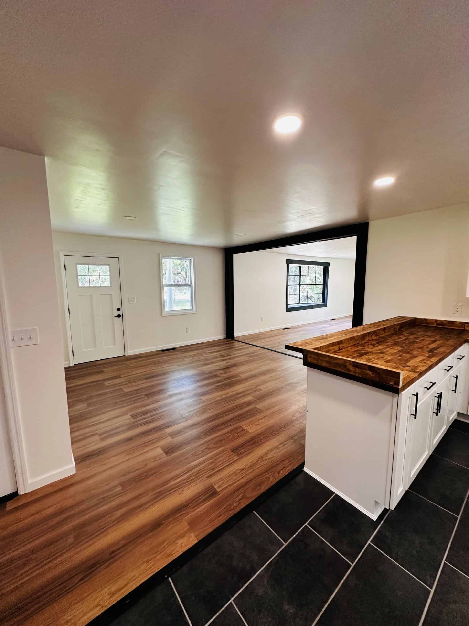 Open concept interior remodel showing kitchen peninsula with butcher block top, LVP living room flooring, black framed opening, and white front door in Knoxville TN