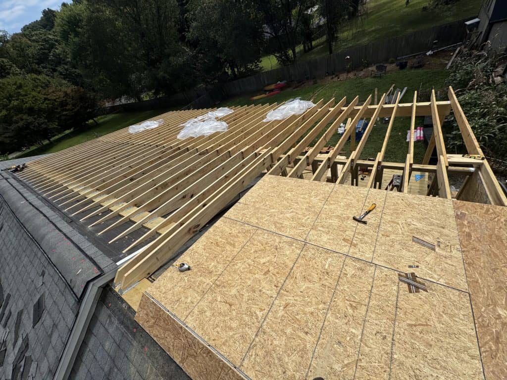Mid-construction view of roof extension with open rafters, partial OSB decking, existing shingle roof, and deck framing in Knoxville Tennessee