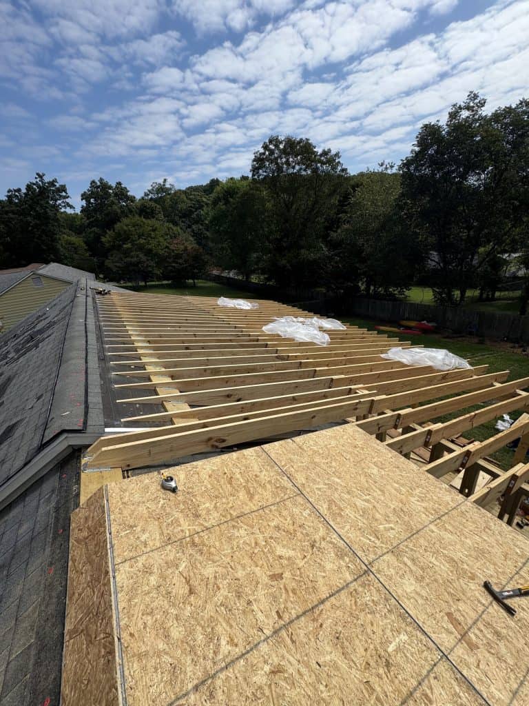 Roof extension rafter framing fully installed before decking on Knoxville TN home by Revival Properties with existing shingle roof visible alongside
