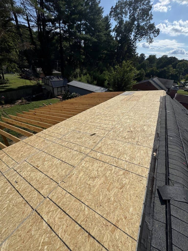 Full OSB decking installation complete on roof extension with exposed rafters and existing shingle roof visible alongside in Knoxville Tennessee