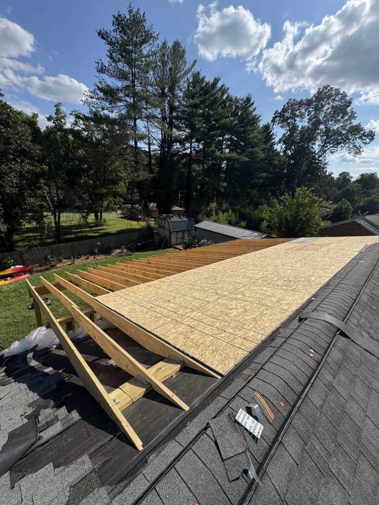 Roof extension rafter framing and OSB decking installation in progress beside existing shingle roof during remodel by Revival Properties in Knoxville TN