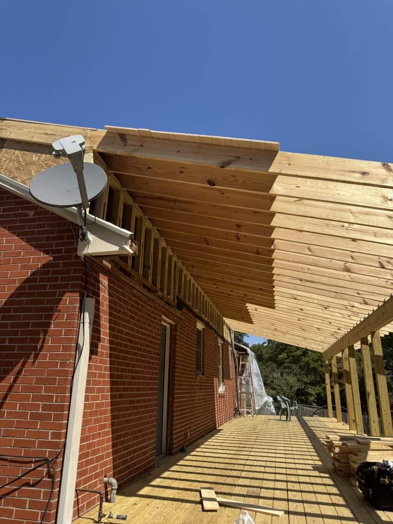 Covered porch roof framing and deck board installation in progress along full length of brick home in Knoxville TN by Revival Properties