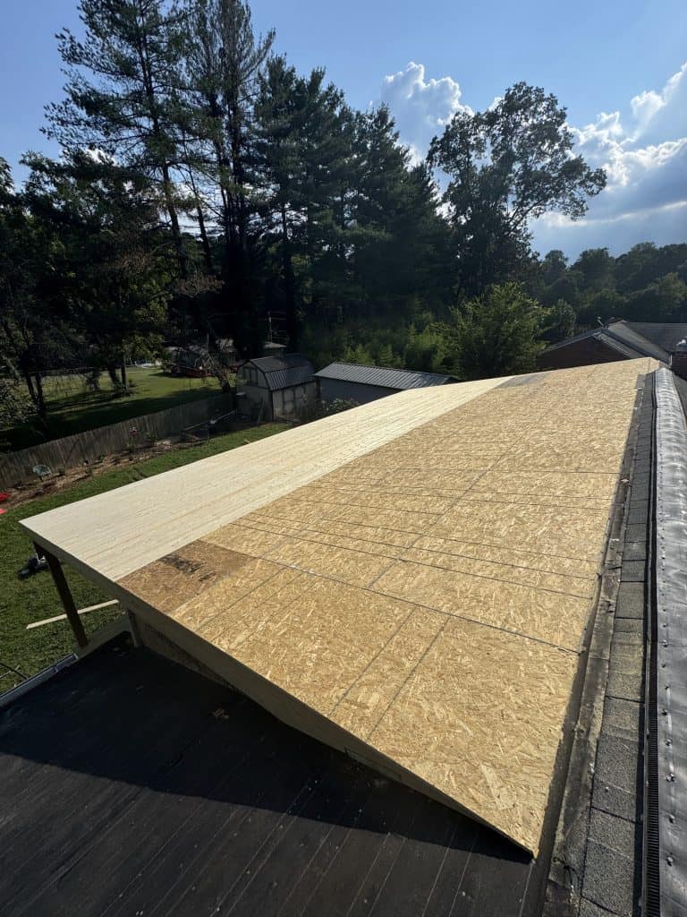 New OSB roof decking installation in progress during roof replacement by Revival Properties in Knoxville TN with existing shingles visible below